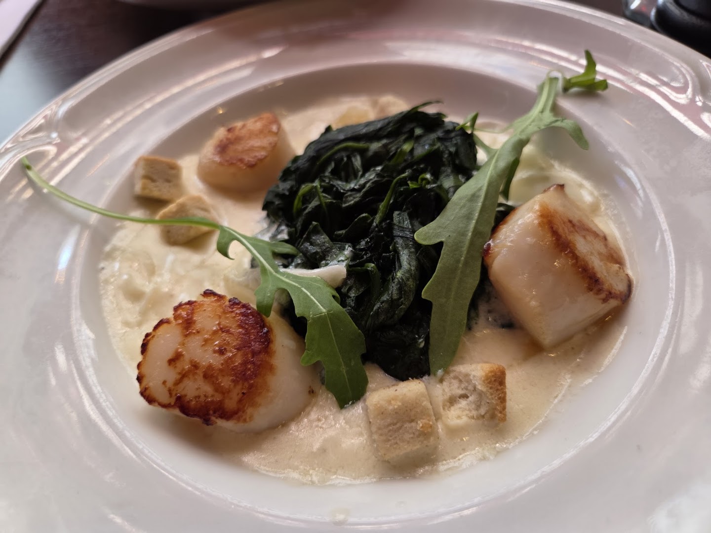 Trois noix de Saint-Jacques, feuilles vertes et sauce dans une assiette claire
